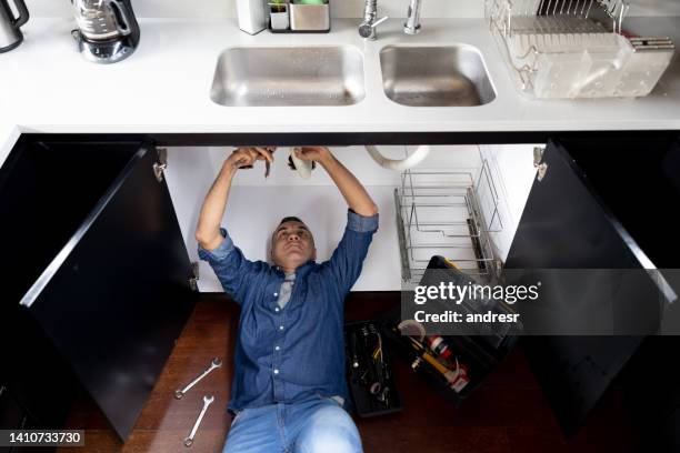 plumber fixing a pipe in the kitchen of a house - kitchen straighten stock pictures, royalty-free photos & images