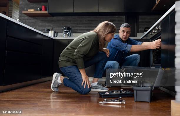 electrician talking to a customer while fixing her over at home - eletrodoméstico imagens e fotografias de stock