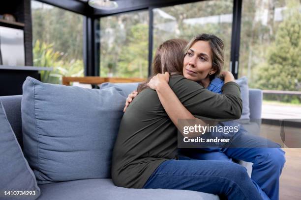 doctor comforting a woman at home and giving her a hug - vulnerability stock pictures, royalty-free photos & images