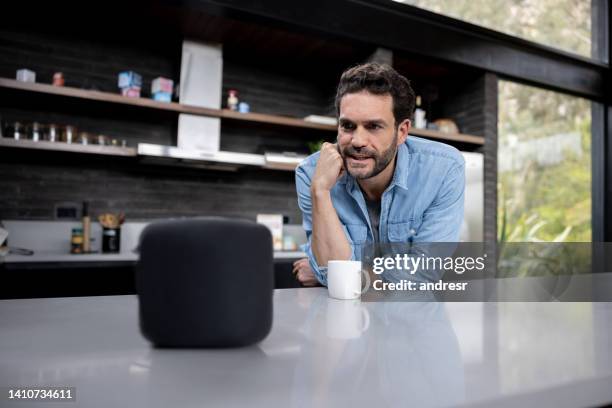 mann zu hause, der mit seinem intelligenten lautsprecher spricht - smart speaker stock-fotos und bilder