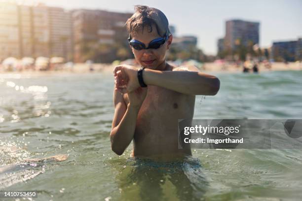 teenager-junge, der seinen fitness-tracker im meer überprüft - junge 13 jahre oberkörper strand stock-fotos und bilder