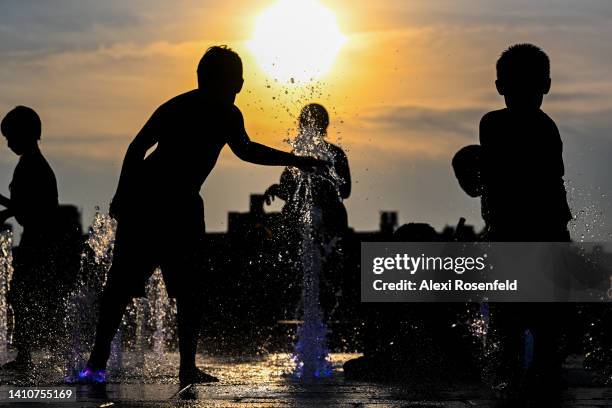 People cool off by playing in a fountain in Domino Park with the Manhattan skyline in the background as the sun sets during a heat wave on July 24,...