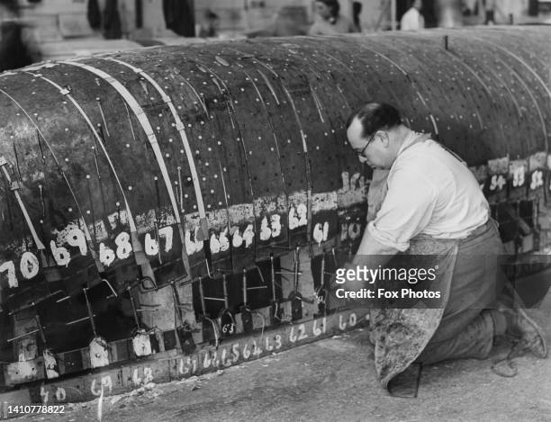 An assembly worker attaches steel bands to the plywood sheet panels to form the shell for one half of the fuselage section of a de Havilland DH98...