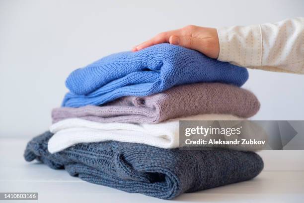 a woman or a girl keeps an armful of knitted things of different colors stacked in a room. warm sweaters for charity. the concept of storage, packaging and washing of handmade products. thrift store, assistance to migrants and refugees. secondary use. - cachemira fotografías e imágenes de stock