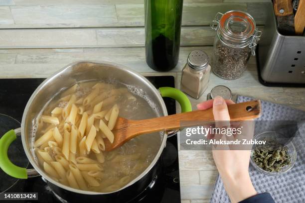 cooking italian pasta at home. a girl or a woman cooks and stirs penne pasta in a saucepan. vegetarian and vegan food. cooking lessons. sustainable development, ethical consumption. step-by-step instructions, do it yourself. step 4. - boiling pan ストックフォトと画像