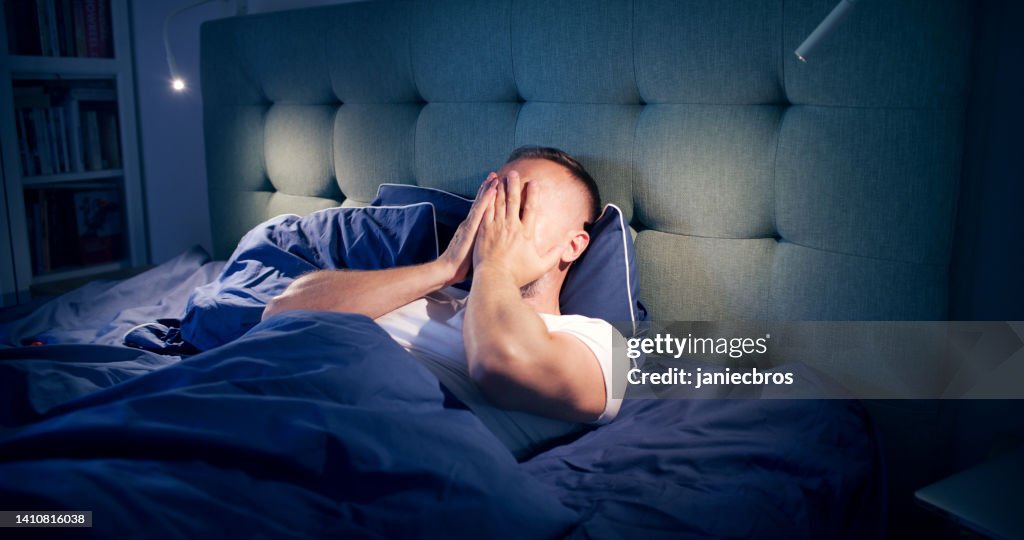 Frustrated man fighting with sleeping disorder. Holding head in hands