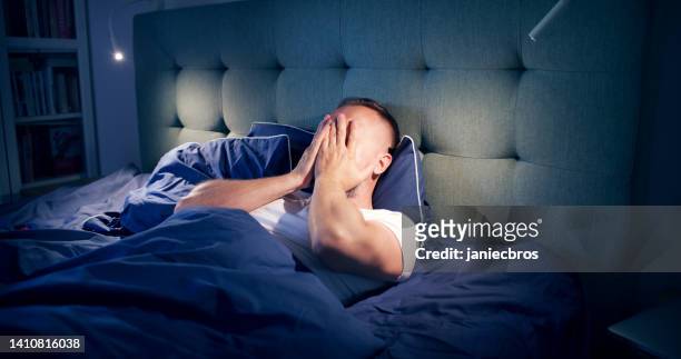 frustrated man fighting with sleeping disorder. holding head in hands - waking up in bed stock pictures, royalty-free photos & images