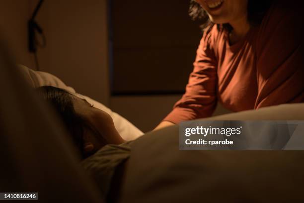 mother putting daughter to sleep - kids sleep in bed stockfoto's en -beelden