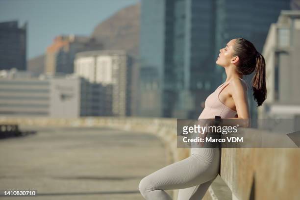 young slim athletic woman resting while on a run for fitness alone in the urban city. one serious sporty and fit female taking a break from a routine outdoor workout and cardio training downtown - center athlete stock pictures, royalty-free photos & images