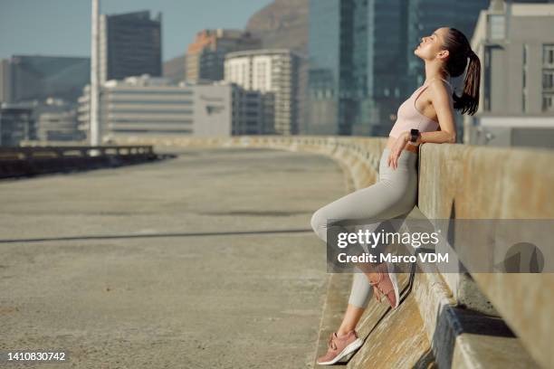 trendy fitness woman resting during run in city. beautiful female athlete taking a break from a cardio workout on a urban bridge on sunny day. sporty athletic girl catching breath after her training - catching breath stock pictures, royalty-free photos & images
