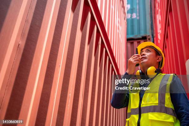 asian dock worker is working in shipping yard while communicate by walkies talkie. logistic and transportation. he is reporting to head office . global business concepts. - funcionário de alfândega imagens e fotografias de stock