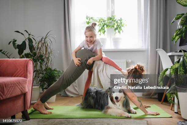 young woman practices yoga with child and dog at home together - chantiers stock-fotos und bilder