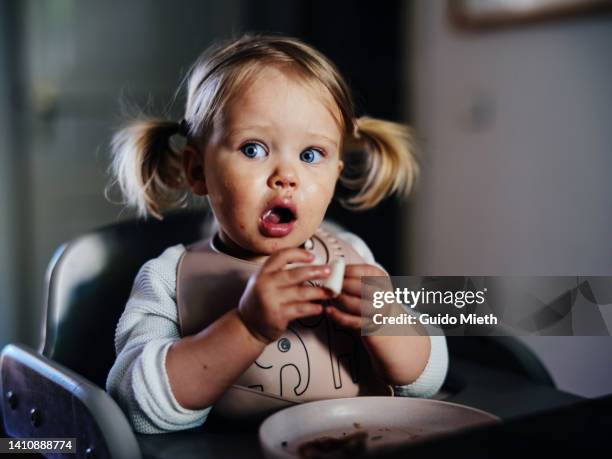 amazed cute toddler girl with pigtails eating at a table at home. - surprise face foto e immagini stock