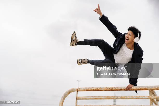 young man leaning on railing while throwing kick in air - man jump outdoor young city stock pictures, royalty-free photos & images