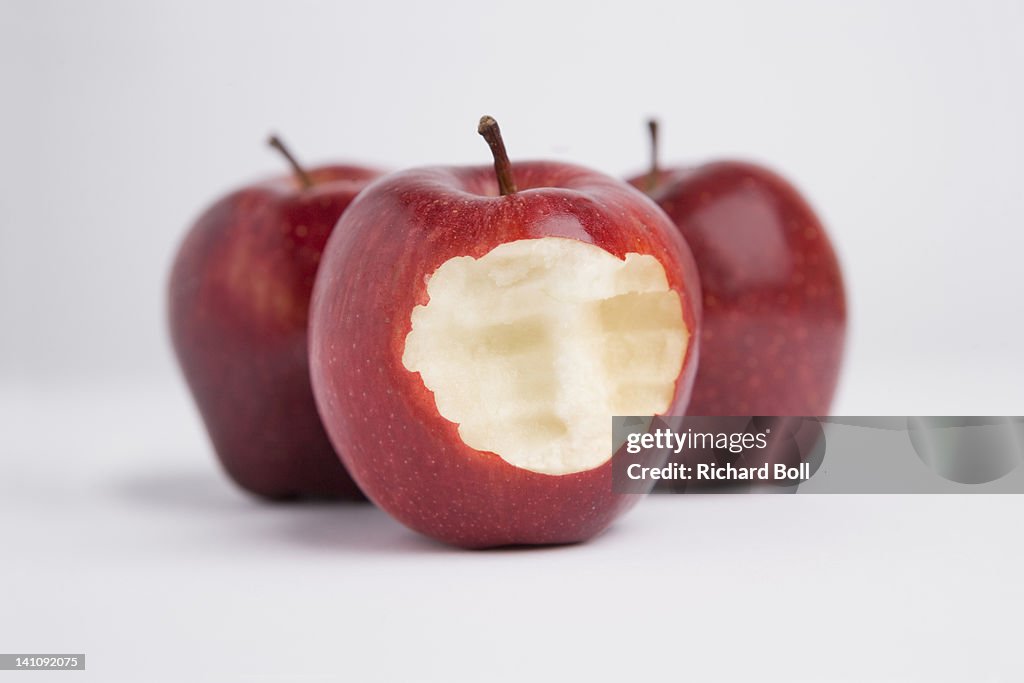 A bite mark in one of three red apples.