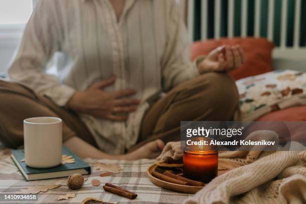 woman sitting on bed in lotus pose with burning candle and tea cup. cozy autumn or winter, hygge lifestyle - chakra bildbanksfoton och bilder