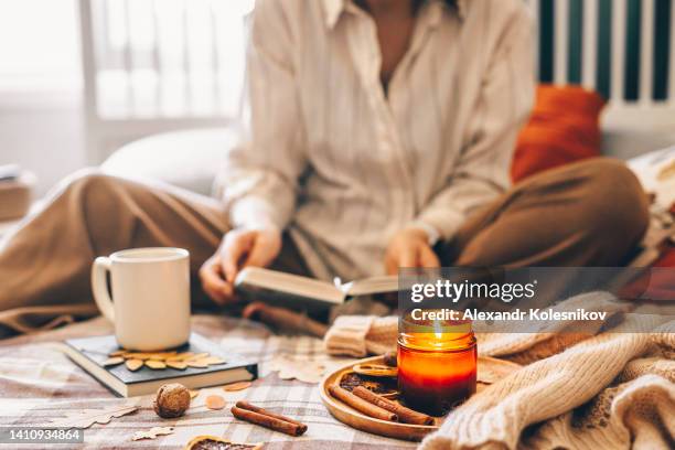 women sitting on bed reading book. mug coffee or tea and wooden tray with burning candle. home decor elements. - cocooning hiver photos et images de collection