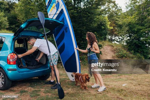 a young loving couple and their dog are preparing for a ride on a lake on a sup board - mens fur boots stock pictures, royalty-free photos & images
