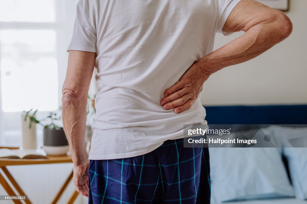 Senior man having back pain, standing in his bedroom.