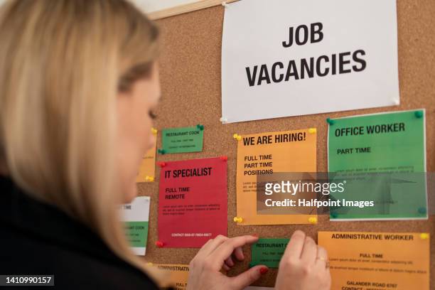 close-up of young volunteer woman pinning job vacancies on bulletin board. rear view. - placa de vaga imagens e fotografias de stock