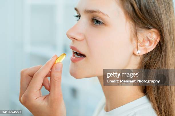 young woman taking pill omega-3 capsule in smiling, close-up - prendere-le-pillole foto e immagini stock