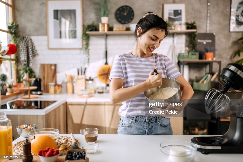Junge schöne Frau, die Kuchenmischung in ihrer heimischen Küche mischt