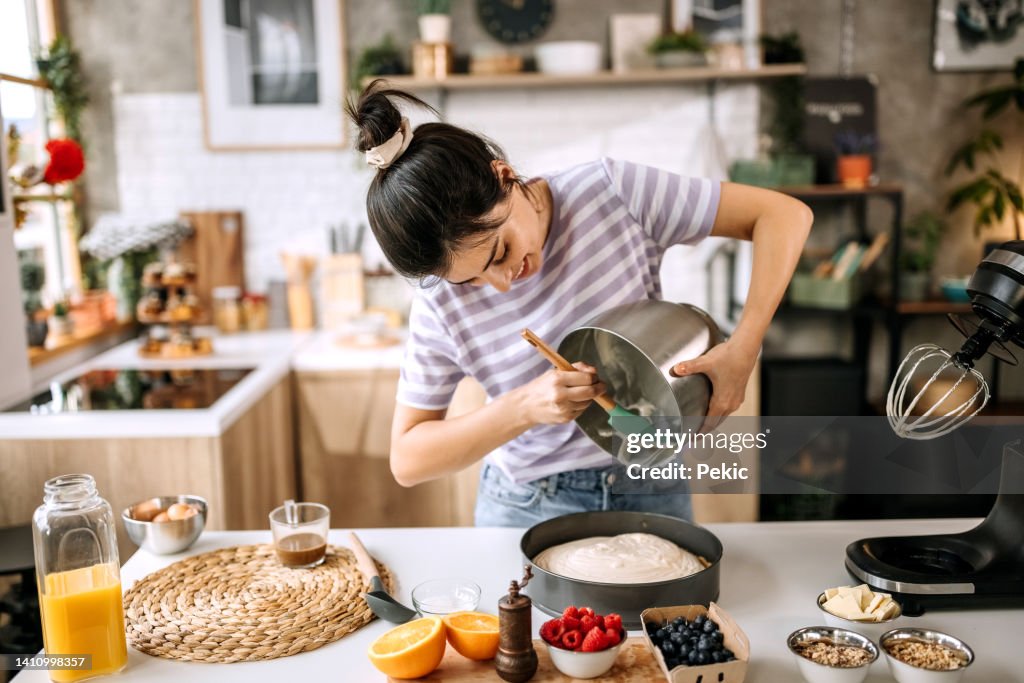 Young beautiful woman pouring cheesecake filling into baking tin