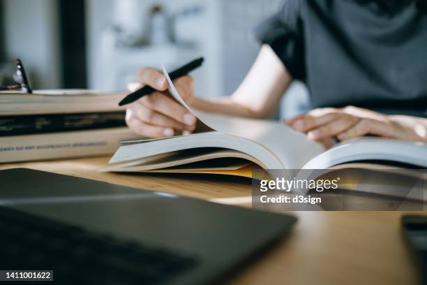 close up. mid-section of young asian woman reading book and making notes at home, concentrates on her studies. further education concept - studie exam stockfoto's en -beelden