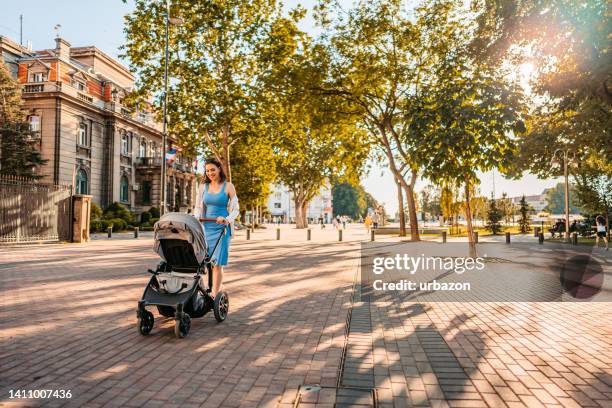 young mother having a walk through the park with her baby - mother stroller stock pictures, royalty-free photos & images
