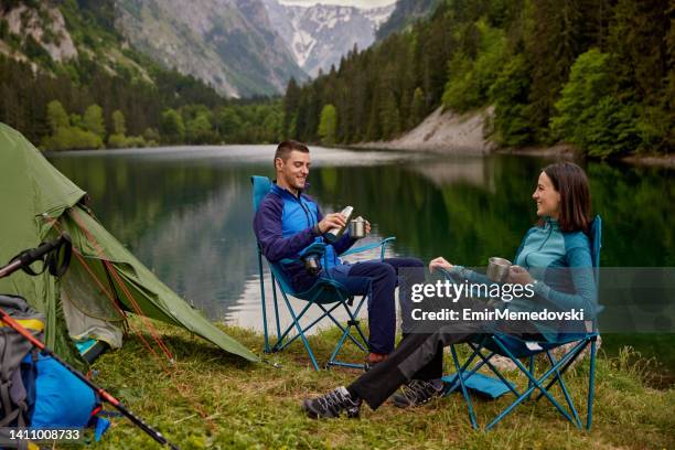 an adventurous young couple at their campsite drinking coffee - camping chair stock pictures, royalty-free photos & images