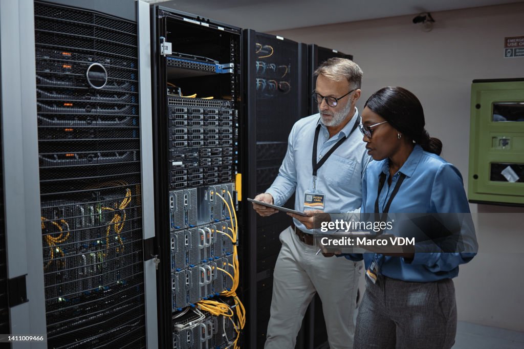 IT technicians using a digital tablet in a server room. Programmers fixing a computer system and network while doing maintenance in a datacenter. Engineers updating security software on a machine
