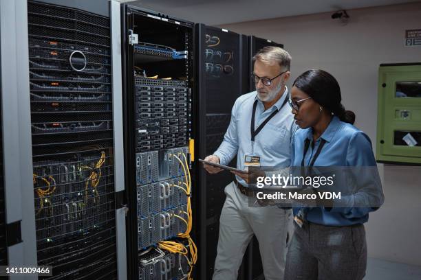 it technicians using a digital tablet in a server room. programmers fixing a computer system and network while doing maintenance in a datacenter. engineers updating security software on a machine - server room 個照片及圖片檔