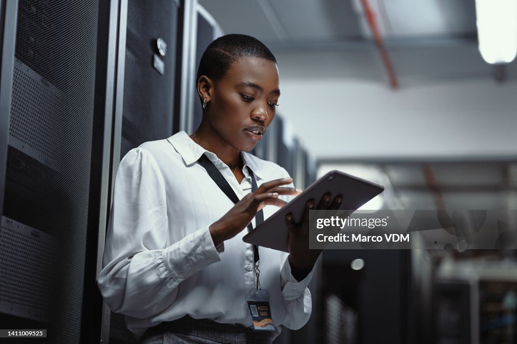 IT technician using a digital tablet in a server room. Female programmer fixing a computer system and network while doing maintenance in a datacenter. Engineer updating security software on a machine
