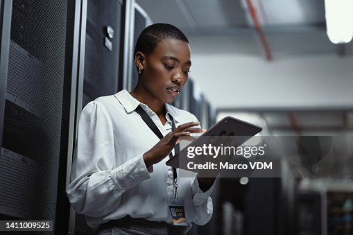 IT technician using a digital tablet in a server room. Female programmer fixing a computer system and network while doing maintenance in a datacenter. Engineer updating security software on a machine IT technician using a digital tablet in a server room. Female programmer fixing a computer system and network while doing maintenance in a datacenter. Engineer updating security software on a machine