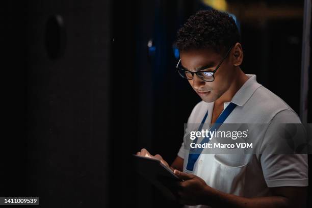 it technician using digital tablet to fix a data centre server mainframe at night. professional computer engineer, developer, programmer thinking, looking confused, coding, repairing malware software - centre de spectacles stockfoto's en -beelden