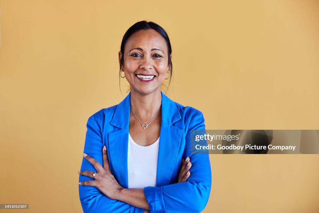 Reife Geschäftsfrau, die lächelt, während sie bei der Arbeit mit verschränkten Armen steht