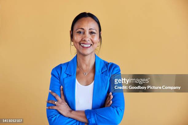 mature businesswoman smiling while standing with her arms crossed at work - yellow background stock pictures, royalty-free photos & images