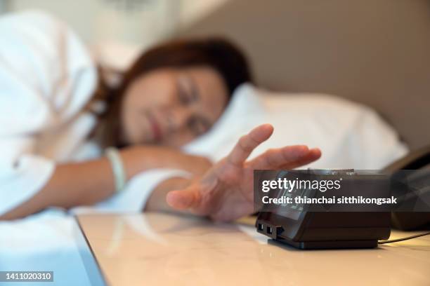 image of woman pressing the stop button on her alarm clock. - alarm stockfoto's en -beelden