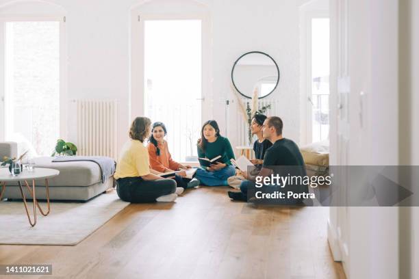 book club members sitting on floor at home and talking - reading books club stockfoto's en -beelden