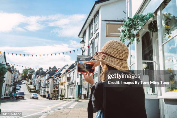 rear view of a young female traveller taking picture of beautiful townscape with smartphone while exploring a town during vacation in summer - uk town stock pictures, royalty-free photos & images