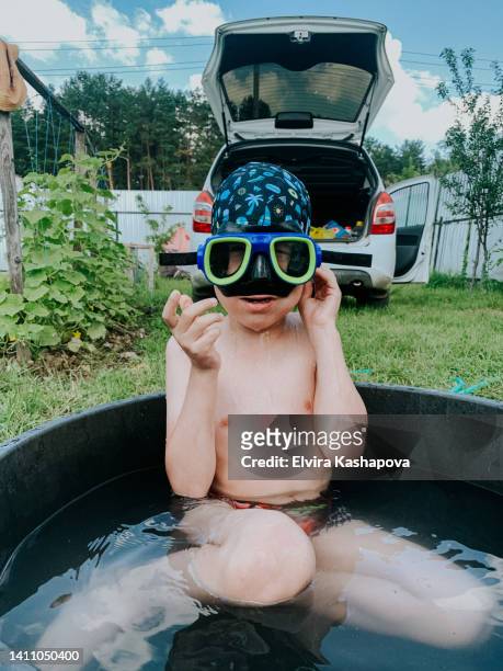 portrait of a boy in a swimming cap and diving goggles sitting outdoors in a basin of water - boy swimming pool goggle and cap stock pictures, royalty-free photos & images