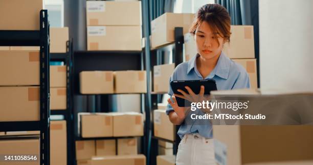 asian businesswoman standing front of shelf use digital tablet check stock on shelf and key data in online information detail in before express delivery at warehouse. - business checklist stock pictures, royalty-free photos & images