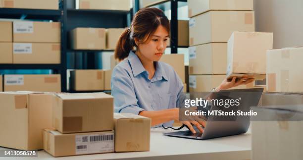 asian businesswoman sit front of shelf use barcode scan customer data in paper box on desk register online code order detail in laptop for express delivery at warehouse. - parcel laptop stock pictures, royalty-free photos & images