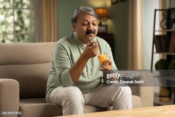 mature man having ice cream sitting on sofa stock photo - sweet food stock pictures, royalty-free photos & images