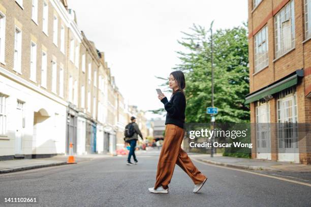 full length of young asian woman with smart phone walking on city street - rush hour stock pictures, royalty-free photos & images