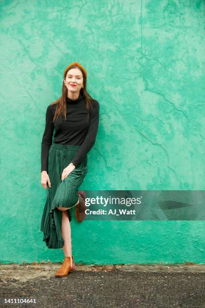 bella giovane donna appoggiata a un muro verde all'esterno - appoggiarsi foto e immagini stock