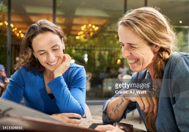 glückliche freundinnen, die in einem café sitzen und auf die menükarte schauen - 2 frauen gespräch ohne männer cafe stock-fotos und bilder
