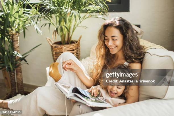 mother and daughter hugging, laughing and looking at photo album. - mother daughter couch imagens e fotografias de stock