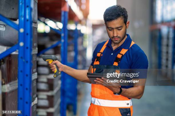 asian male warehouse worker looking at a digital tablet and using a barcode scanner read the information tag labels to compare inventory data information in a factory warehouse. - labeling data stock pictures, royalty-free photos & images