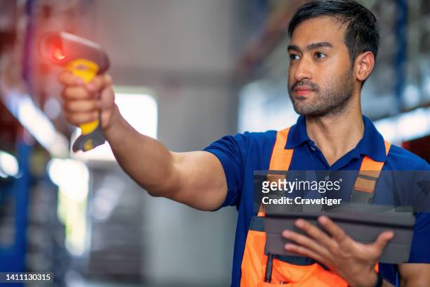 asian male warehouse worker looking at a digital tablet and using a barcode scanner read the information tag labels to compare inventory data information in a factory warehouse. - rfid stock-fotos und bilder